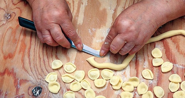 Orecchiette being shaped by hand with a knife on a wooden board