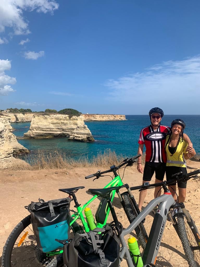 Two cyclists with rental e-bikes on the rocky coast of Puglia